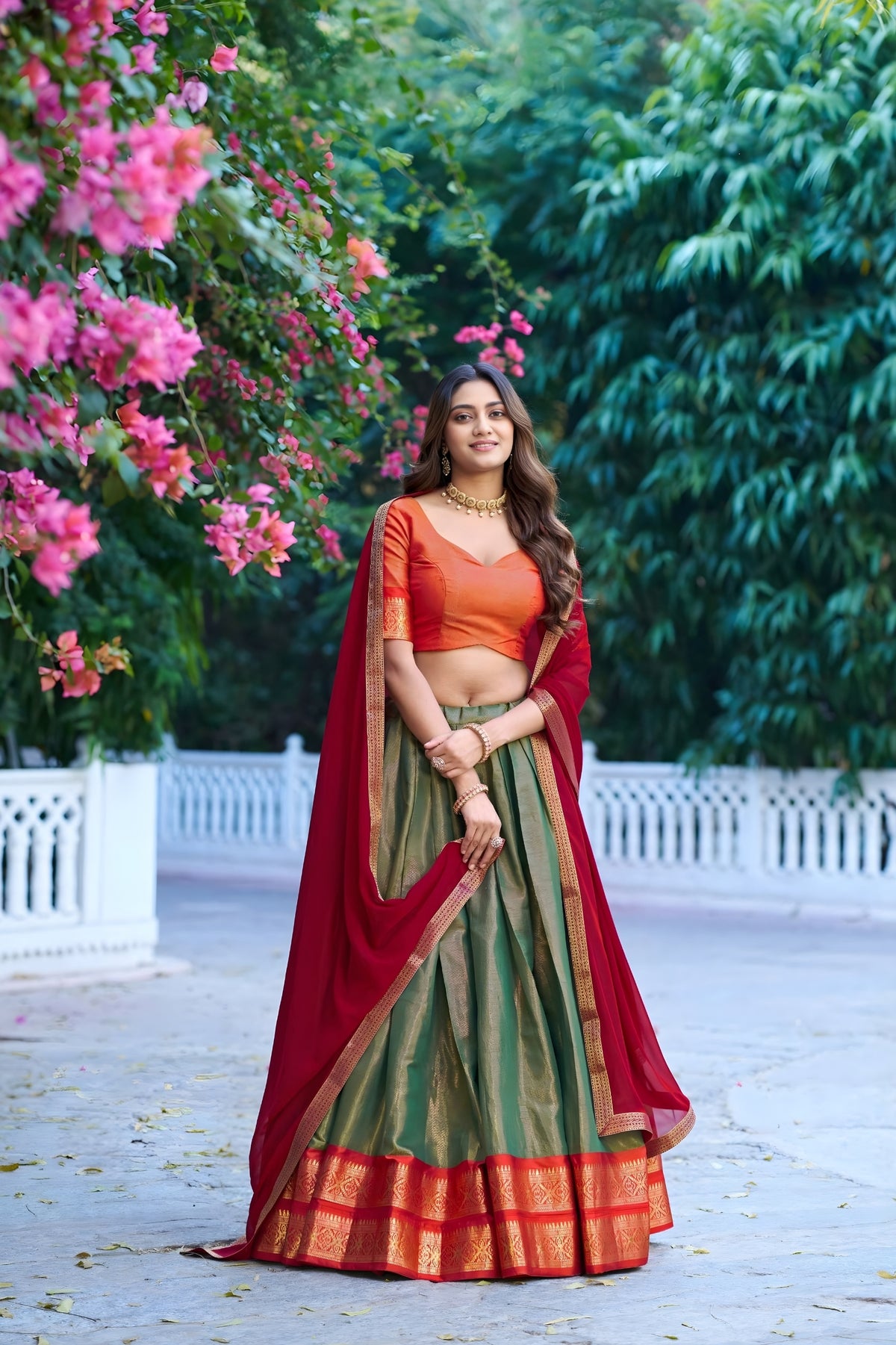 Woman in traditional Indian attire standing in a garden with pink flowers and greenery.