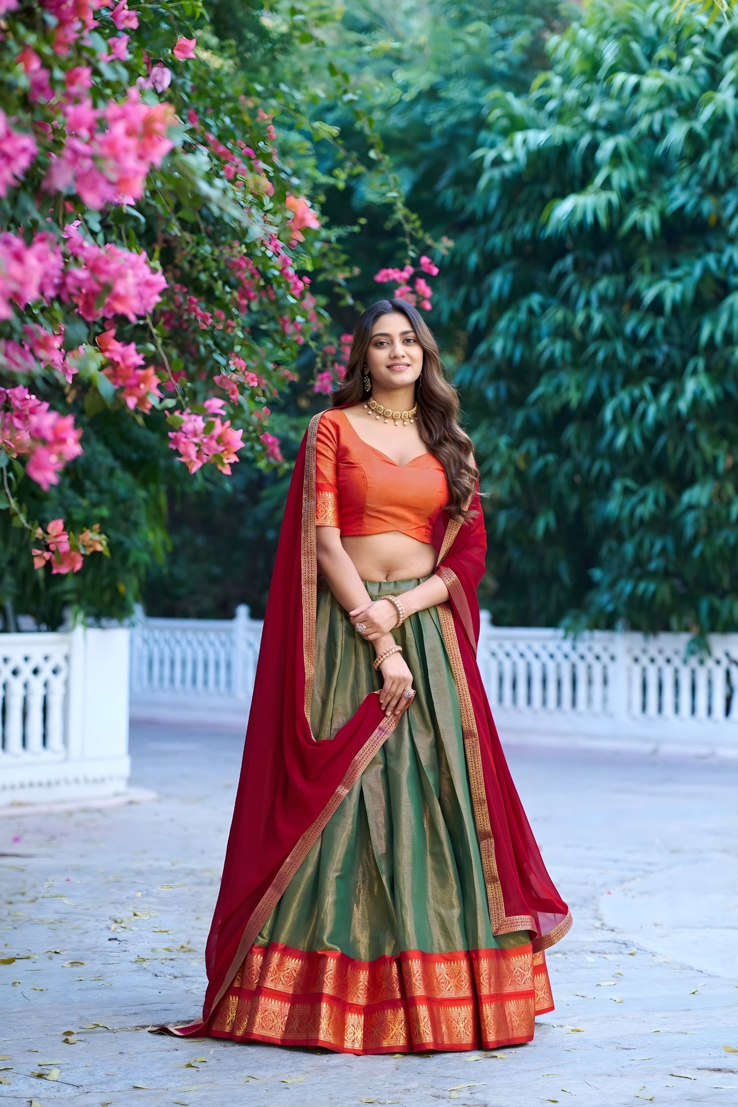 Woman in traditional Indian attire standing in a garden with pink flowers and greenery.