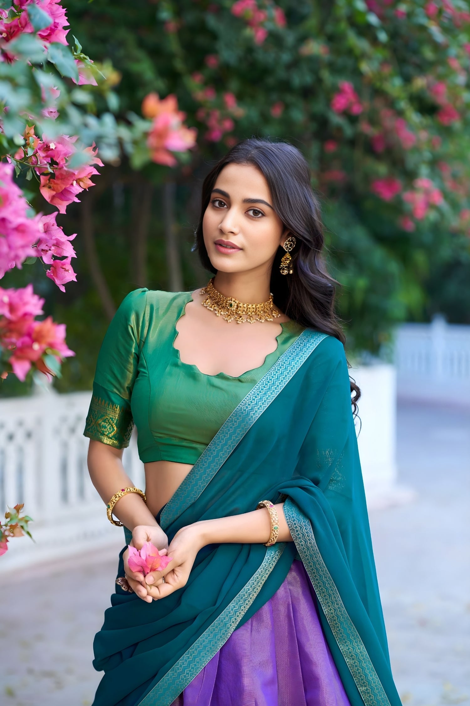 Woman in a green and purple traditional outfit standing in front of pink flowers.