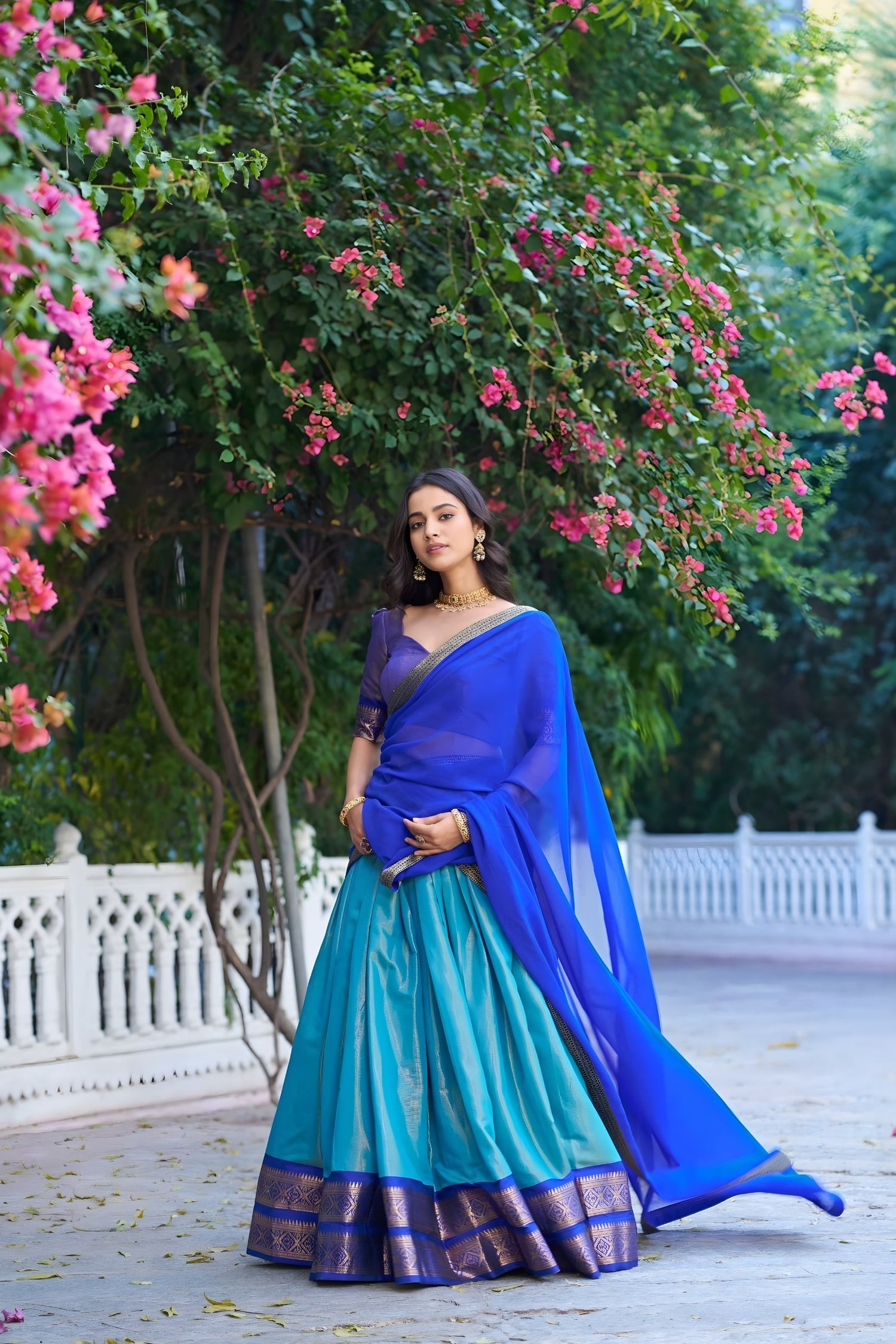 Woman in a blue and green saree standing in front of a flowering tree