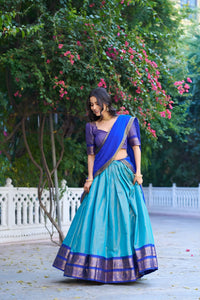 Woman in a blue and purple traditional outfit standing in a garden with greenery and flowers.