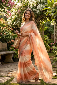 Woman in a peach saree standing in a garden with flowers and a bench in the background