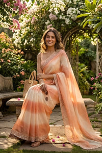 Woman in a peach saree sitting in a garden with flowers and a bench.