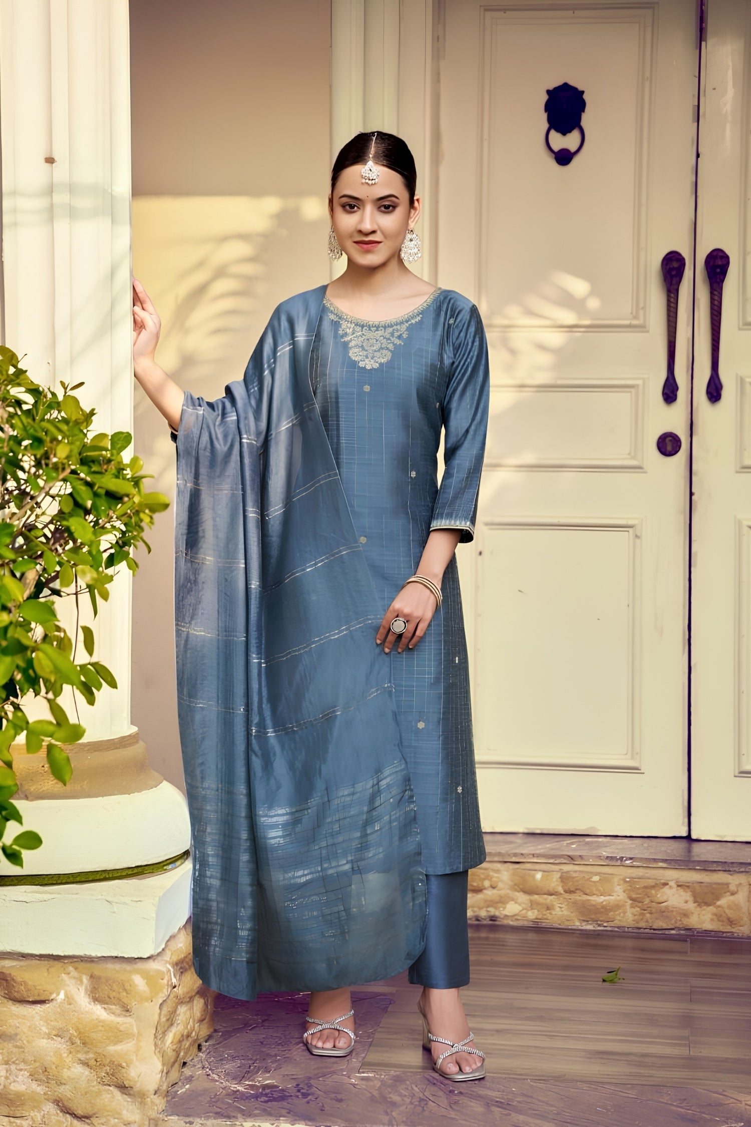 Woman in a blue traditional outfit standing in front of a white door.