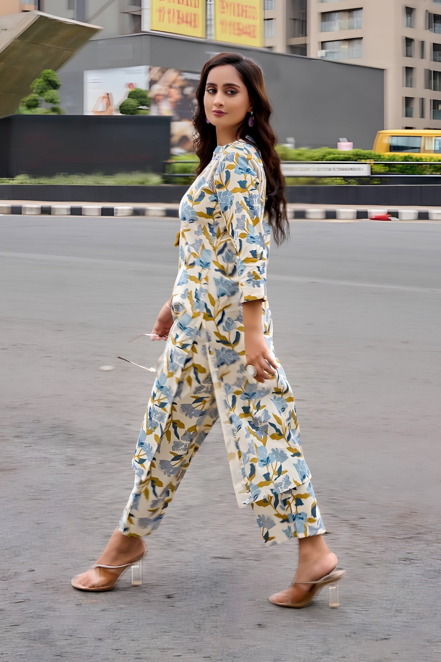 Woman in a floral outfit walking on a road with buildings and vehicles in the background