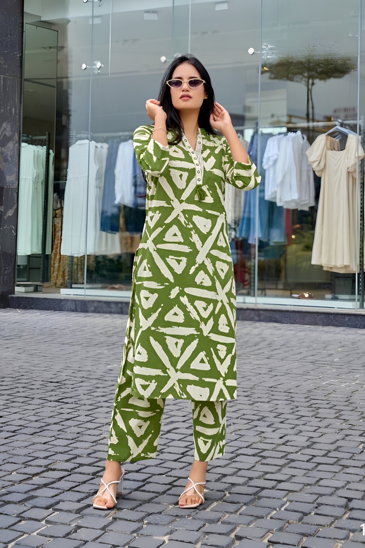 Woman wearing a green and white patterned outfit standing on a street with a clothing store in the background.