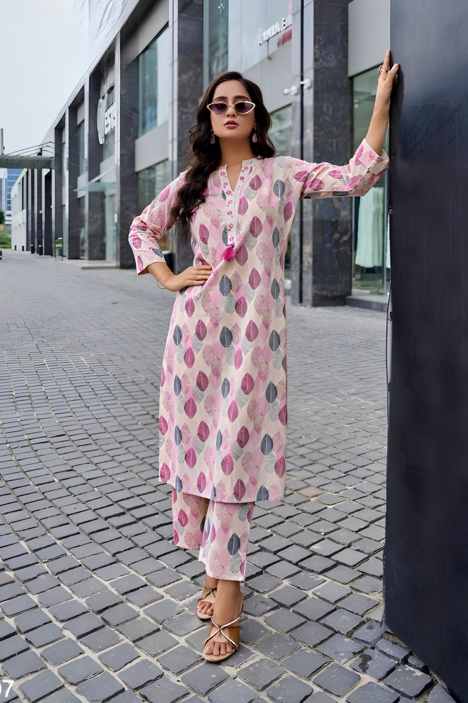 Woman in a pink and white patterned outfit standing on a city street.
