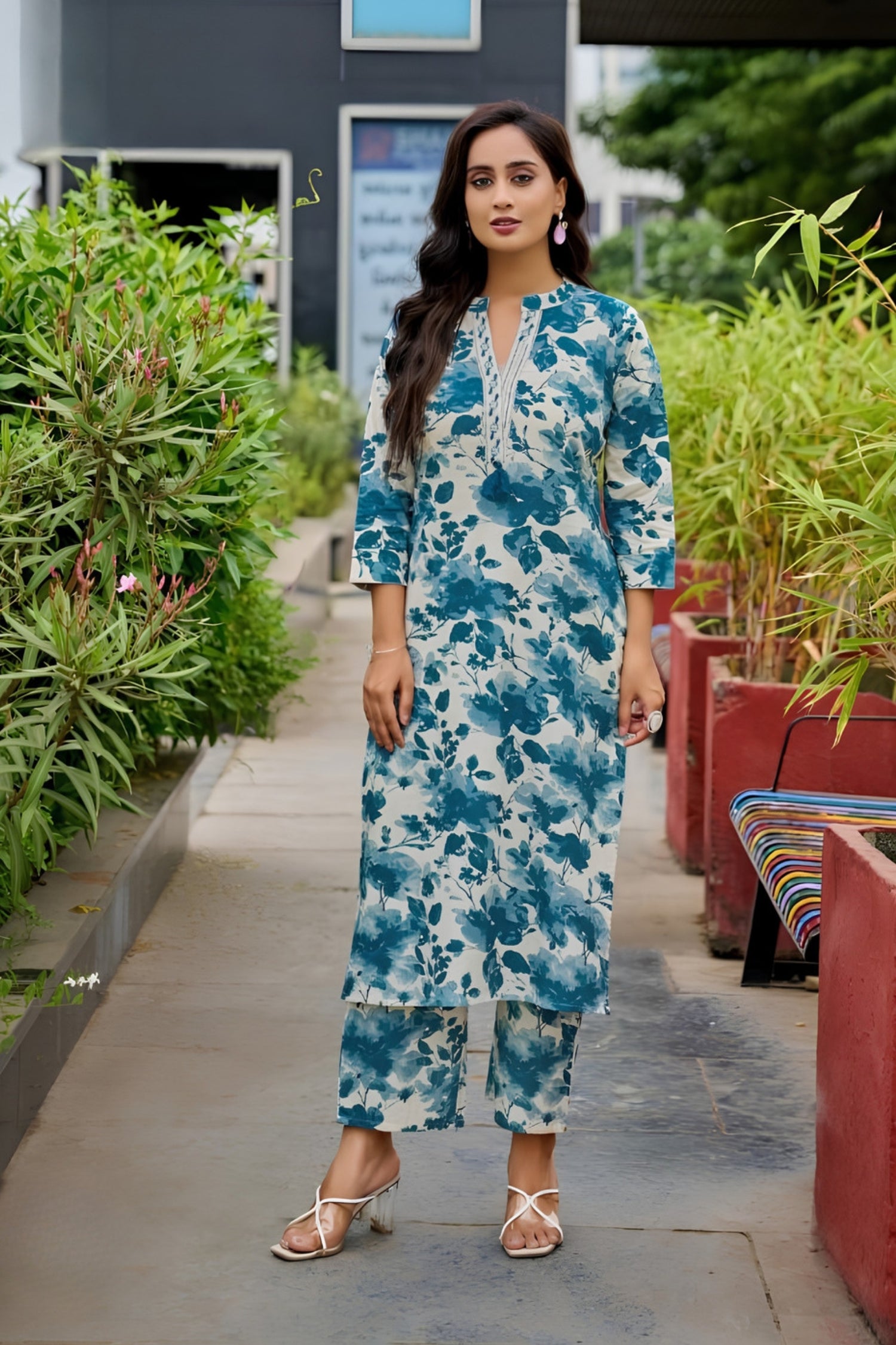Woman in a blue floral dress standing outdoors with greenery around