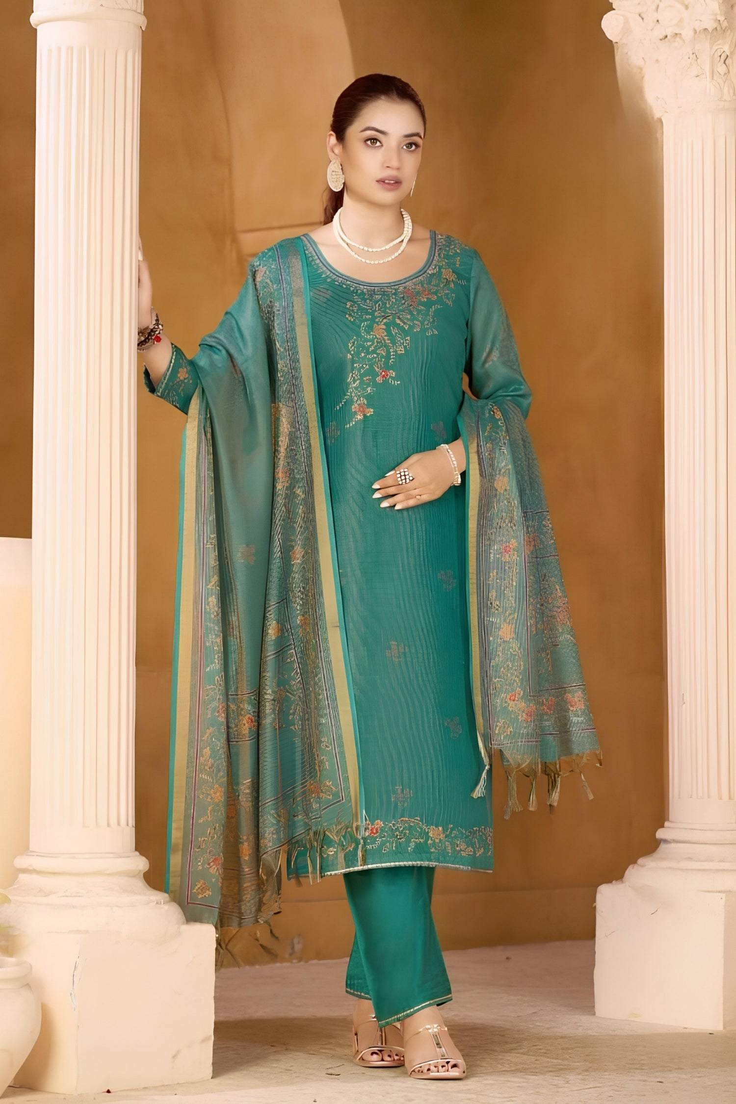 Woman in a teal embroidered traditional outfit standing between two columns.