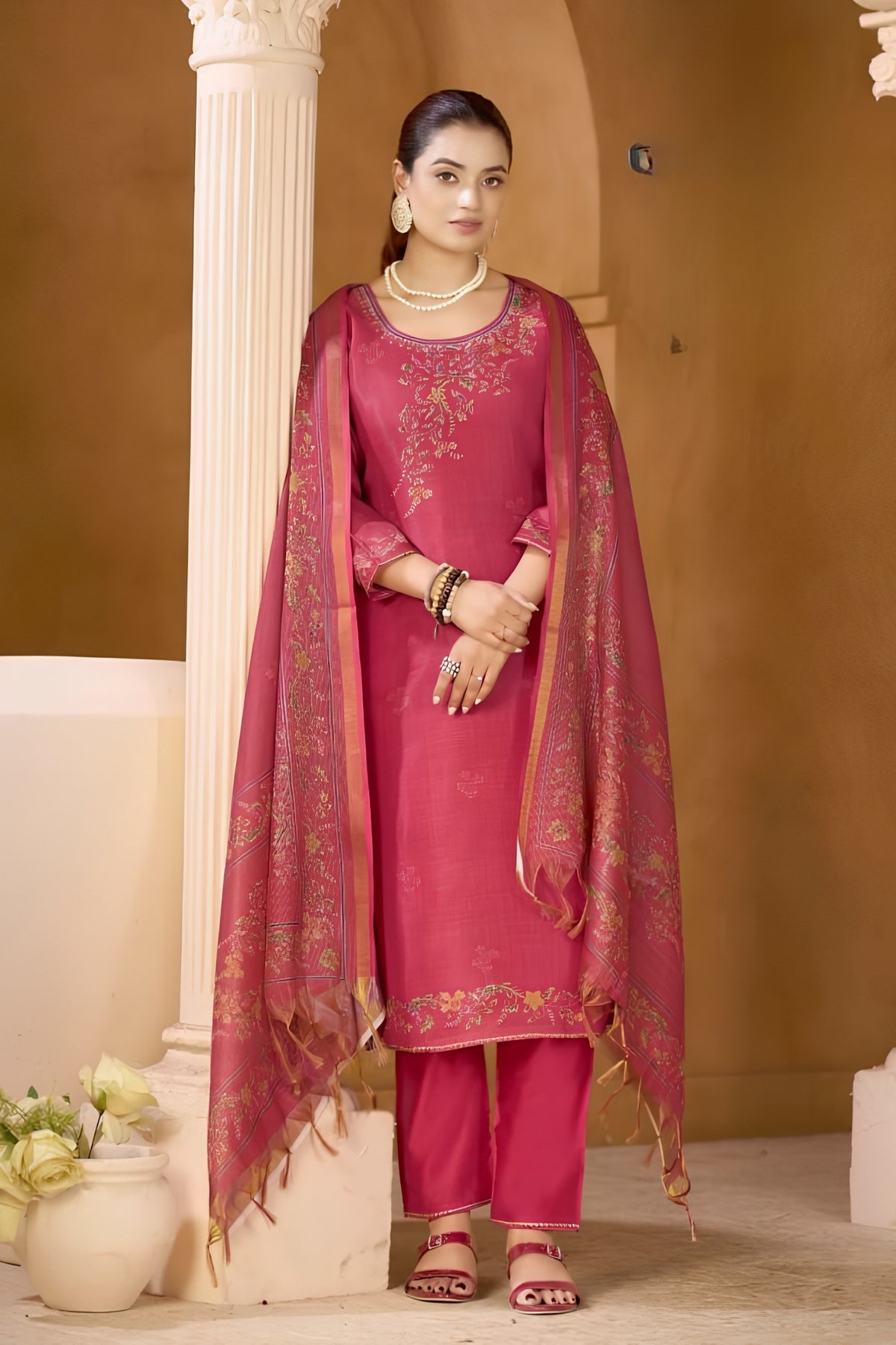 Woman in a pink traditional outfit with a matching dupatta standing against a beige wall.