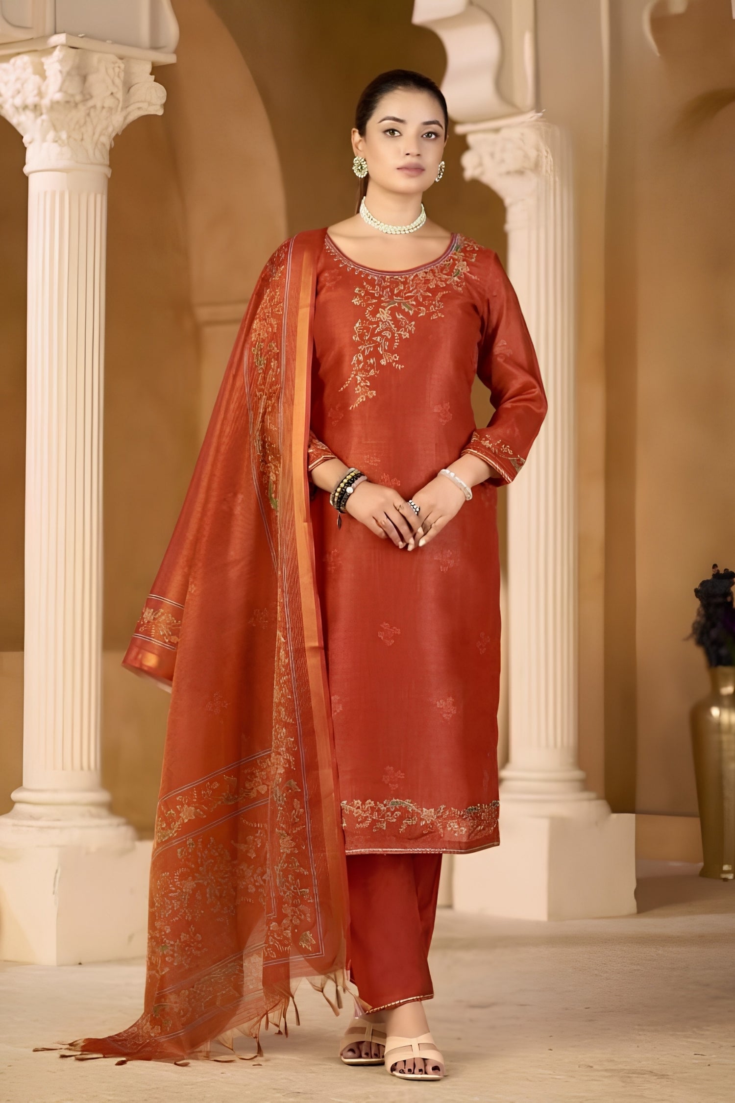 Woman in a traditional red outfit with a dupatta standing in an elegant interior setting.