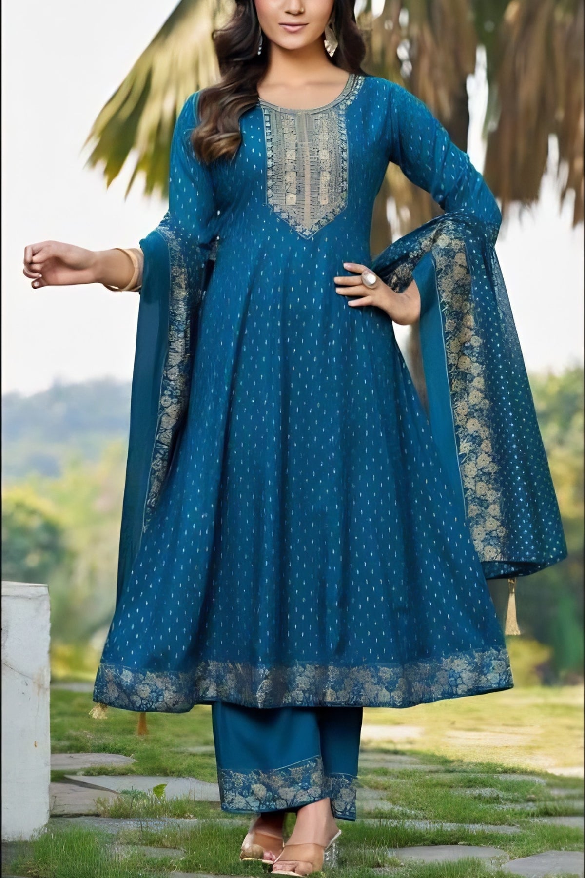 Woman wearing a blue traditional outfit with intricate patterns in an outdoor setting.
