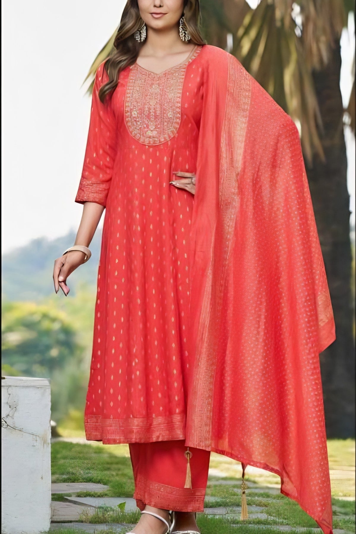 Woman wearing a red traditional outfit with a matching dupatta in an outdoor setting.
