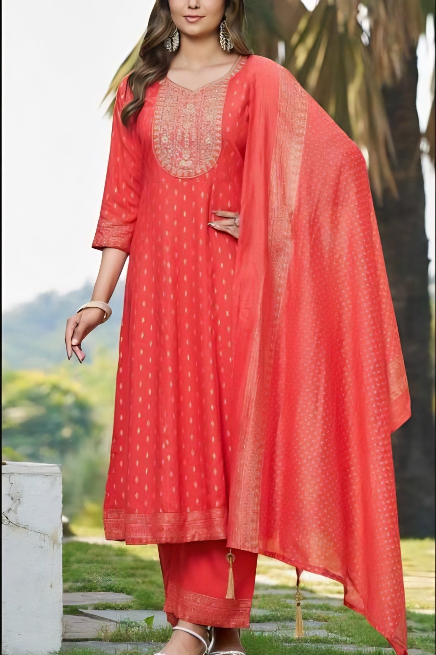 Woman wearing a red traditional outfit with a matching dupatta in an outdoor setting.