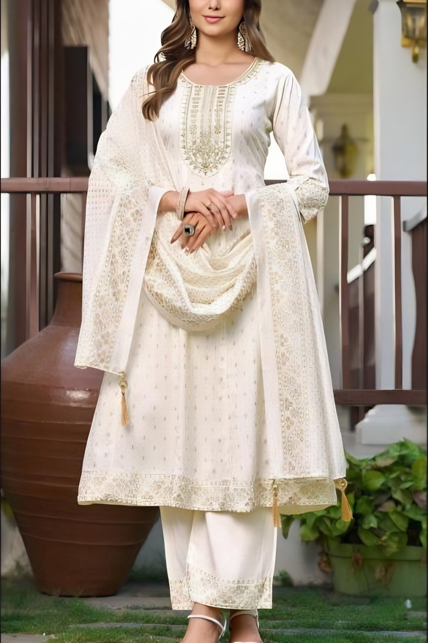 Woman wearing a white embroidered traditional outfit with a dupatta, standing outdoors.